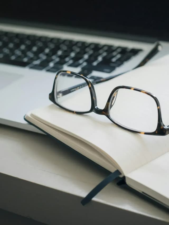 Glasses on an open notebook beside a laptop.