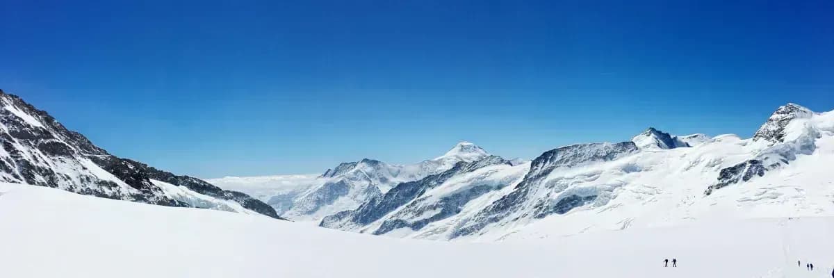 Snow-covered mountains with a clear blue sky and distant trekkers